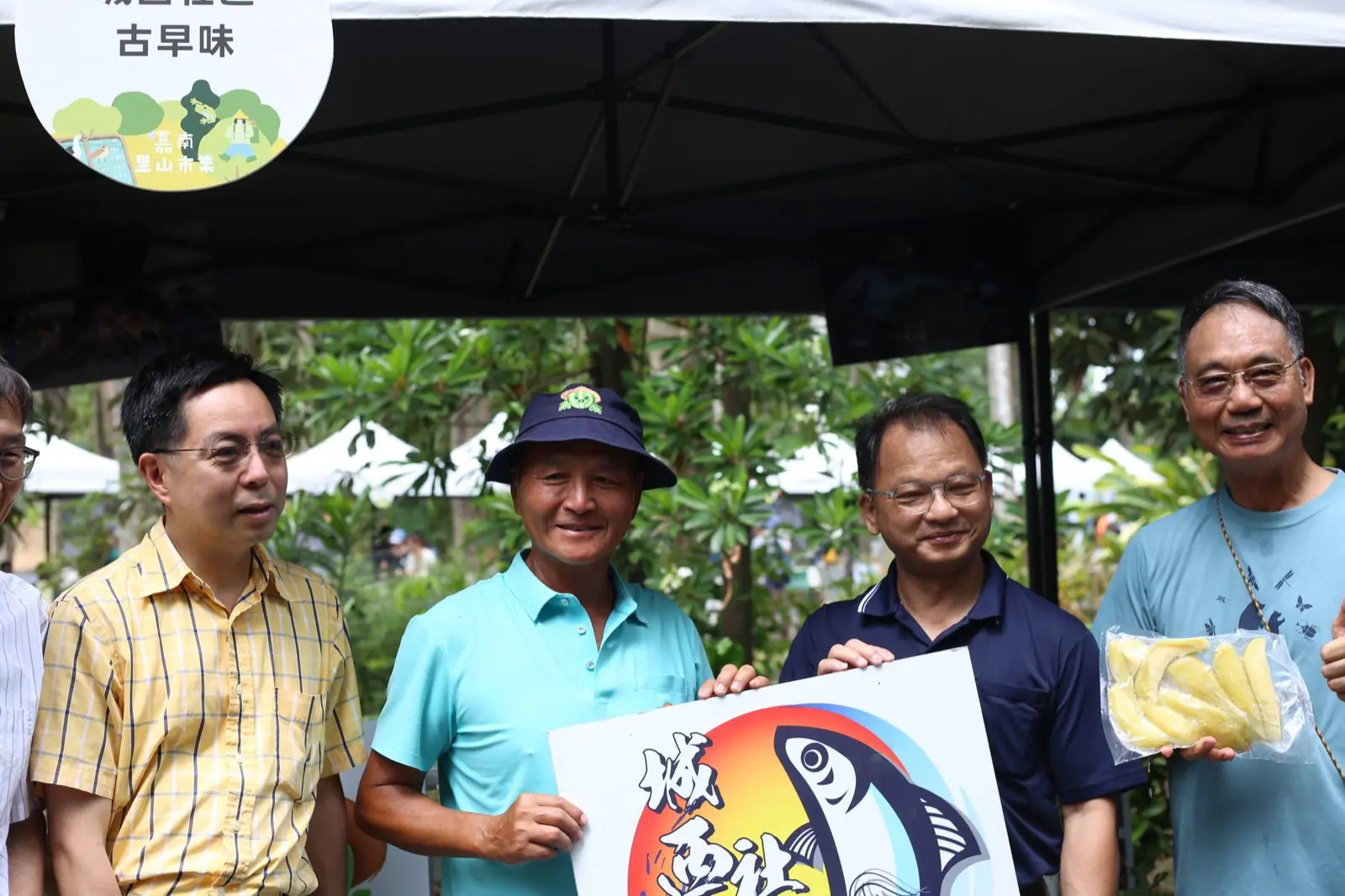 長官貴賓於市集攤位前與攤商合影，攤位圓牌印有嘉南里山市集主視覺
