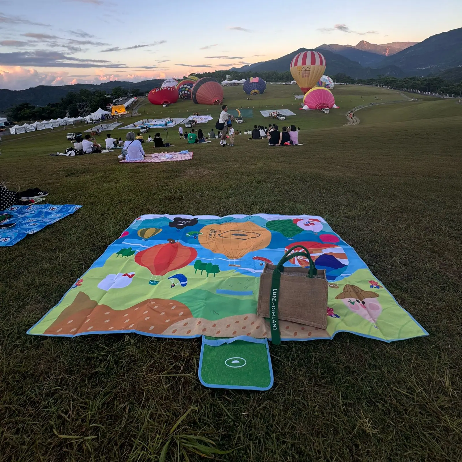 野餐墊鋪展於鹿野高台熱氣球嘉年華現場,遠方多顆熱氣球升空